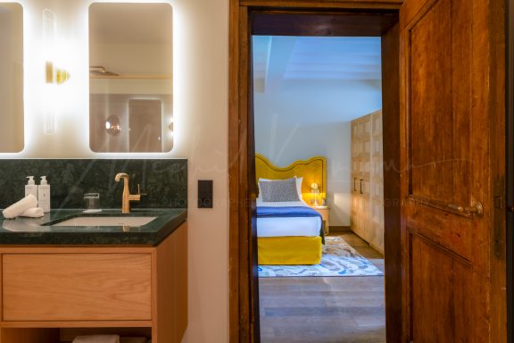 Badkamer met wastafel, verlichte spiegel en doorkijk naar de hotelkamer — projectfotografie voor Wolffs Kitwerken